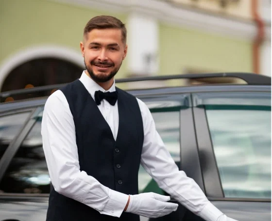 Uniformed chauffeur in white gloves welcoming guests beside a black luxury vehicle