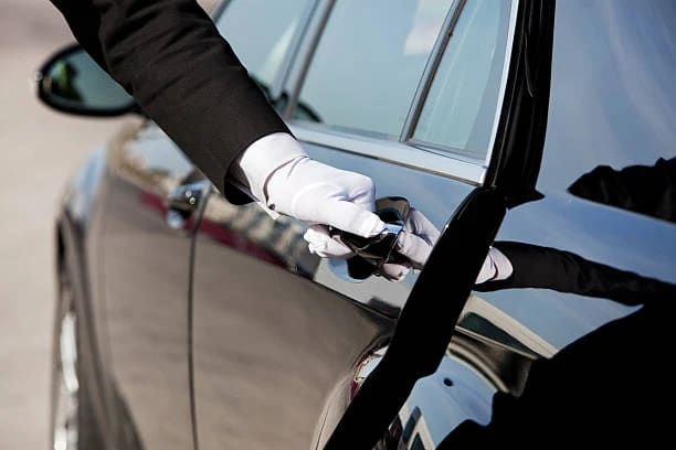Chauffeur in formal attire opening the door of a black luxury sedan